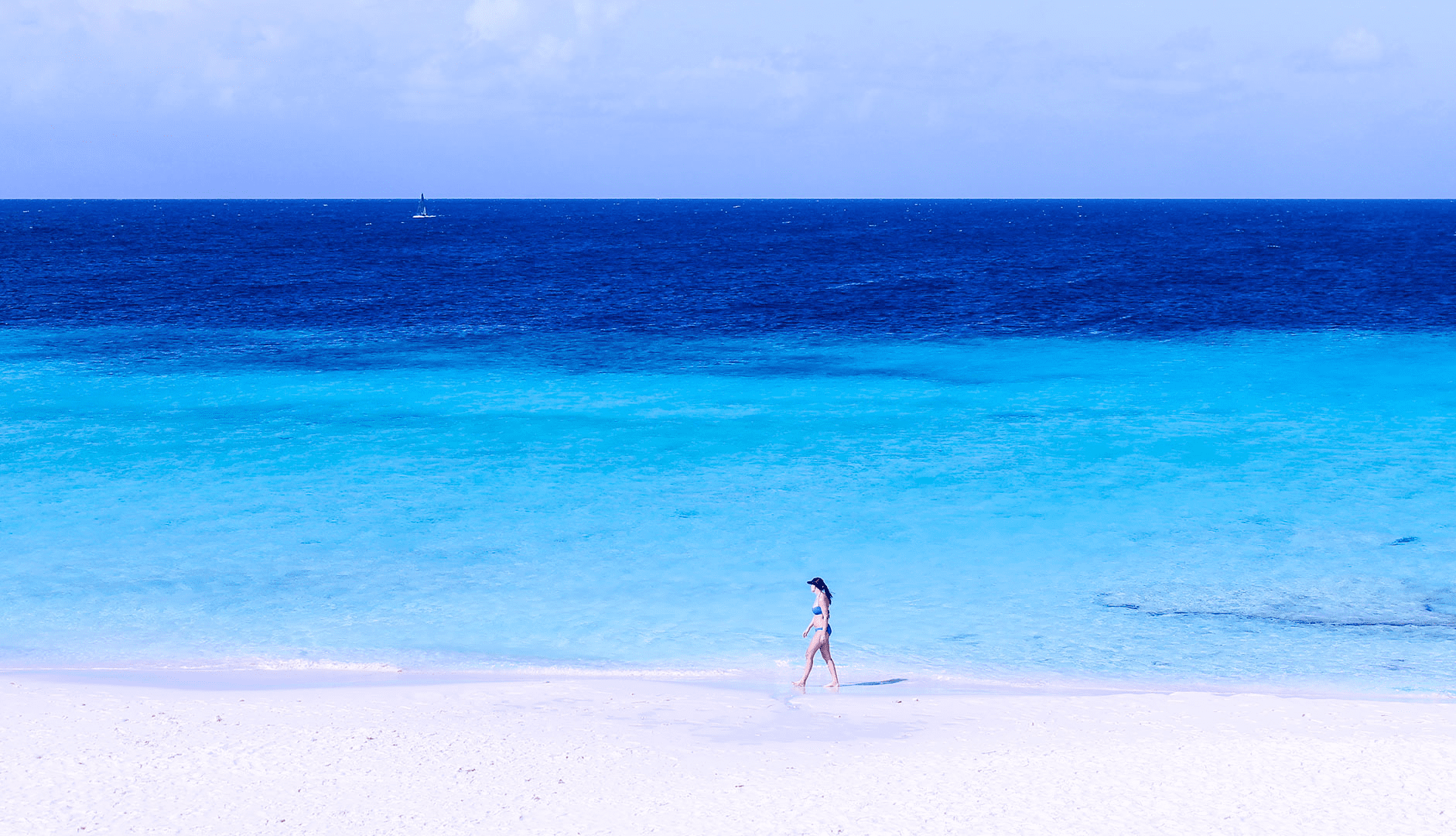 A guest walking along a white-sand beach by a vacation rental